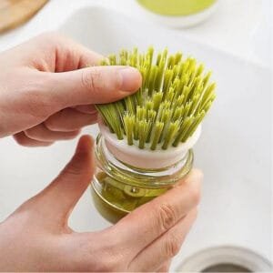 Cepillo lavavajillas Alemka en acción – Cerdas de nailon firmes y duraderas Manos sujetando cepillo lavavajillas Alemka de color verde con cerdas firmes y mango ergonómico