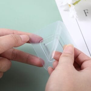"Preparación del gancho adhesivo para instalación en superficie lisa" Manos retirando la película protectora de un gancho adhesivo antes de instalar